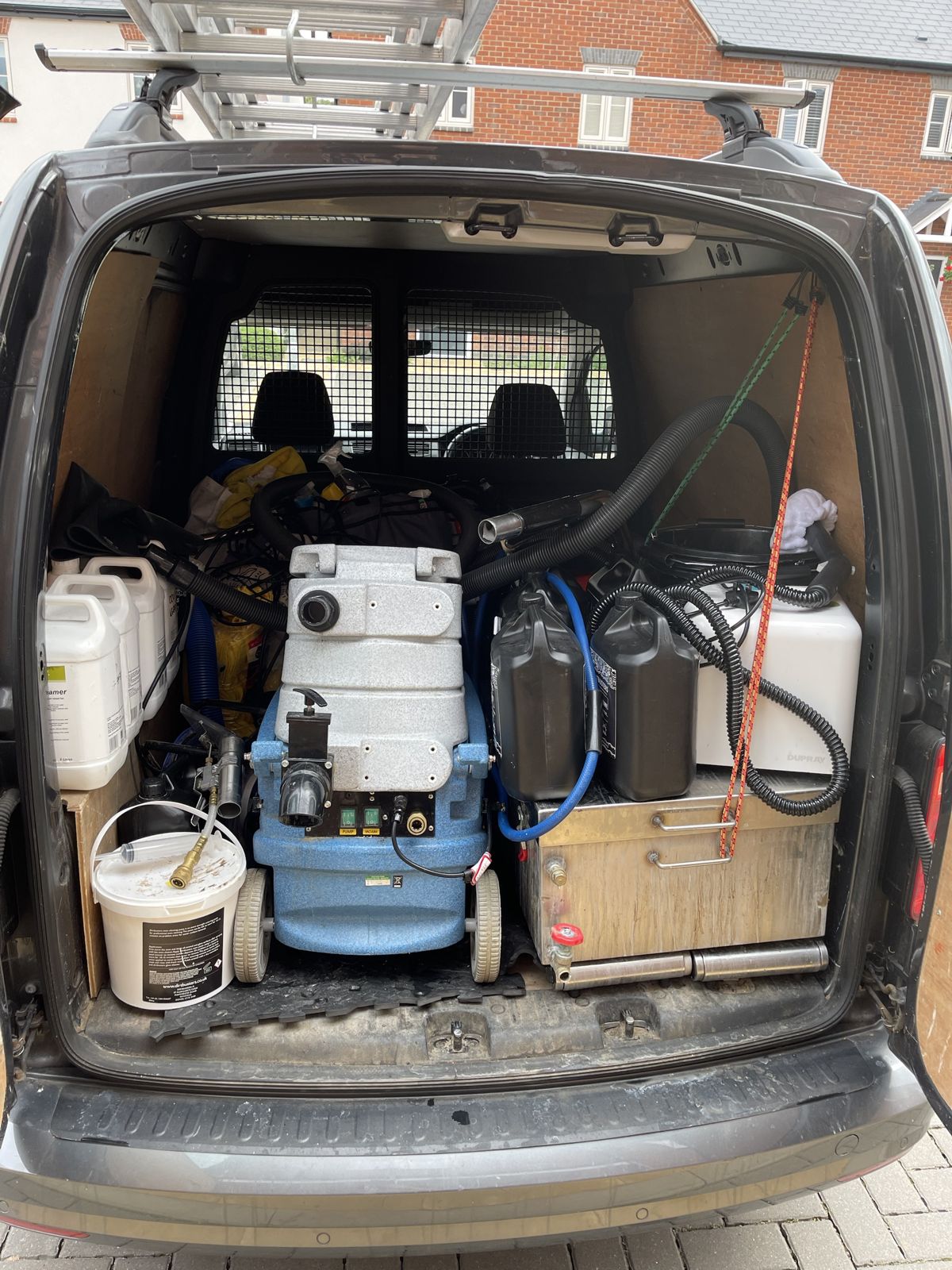 A branded cleaning van parked up, with a carpet machine loaded in the back