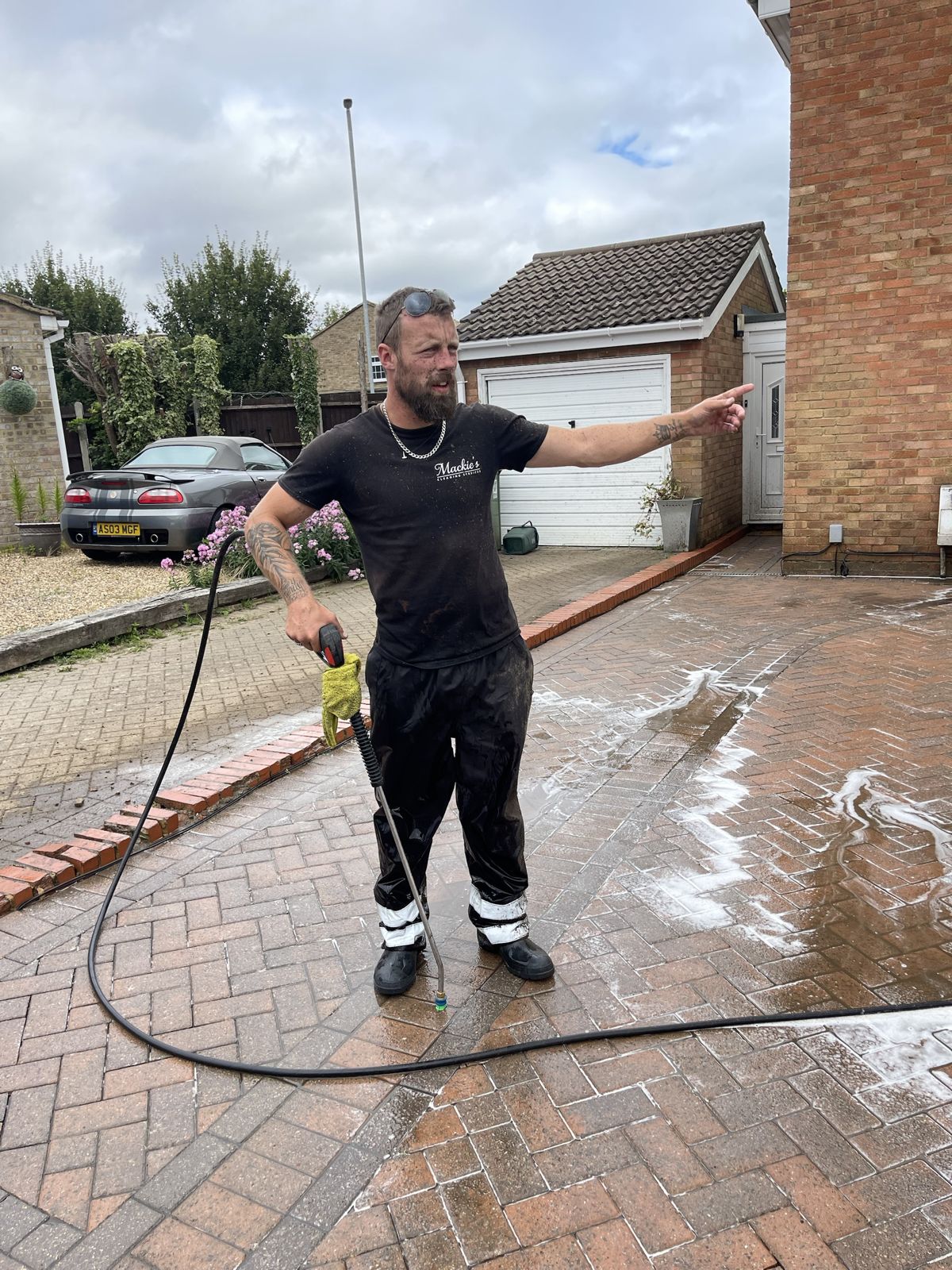A cleaner pressure washing a driveway and pointing at the clean line