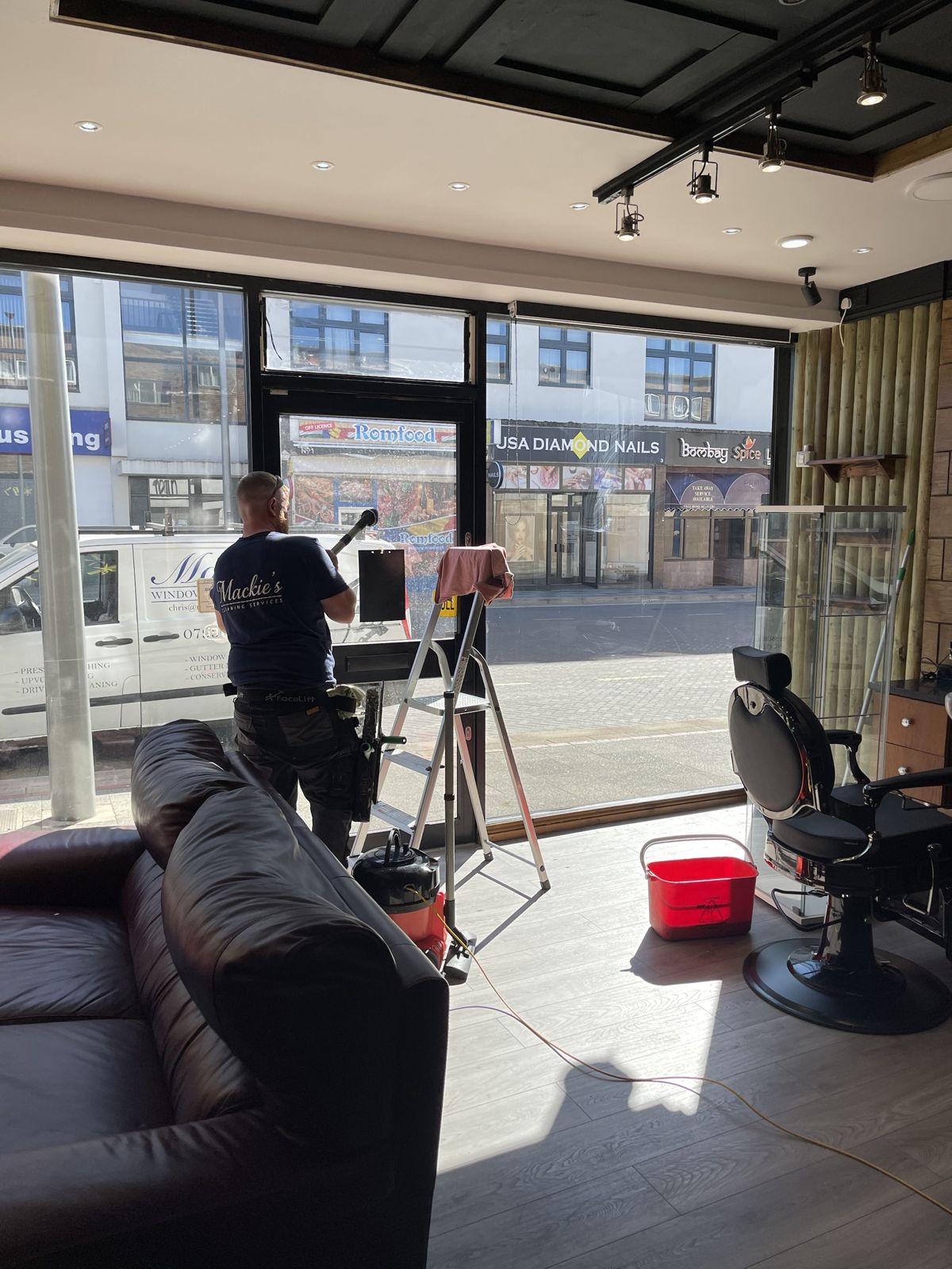 A cleaner working on the inside of a shopfront window, the high street visible outside